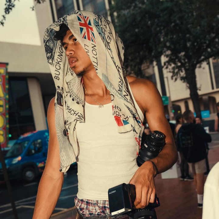 Jonathan Platt on a city street with a scarf over his head, holding two cameras